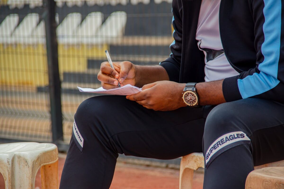 services-img-02 A coach writing notes on the sidelines during an outdoor sports match.
