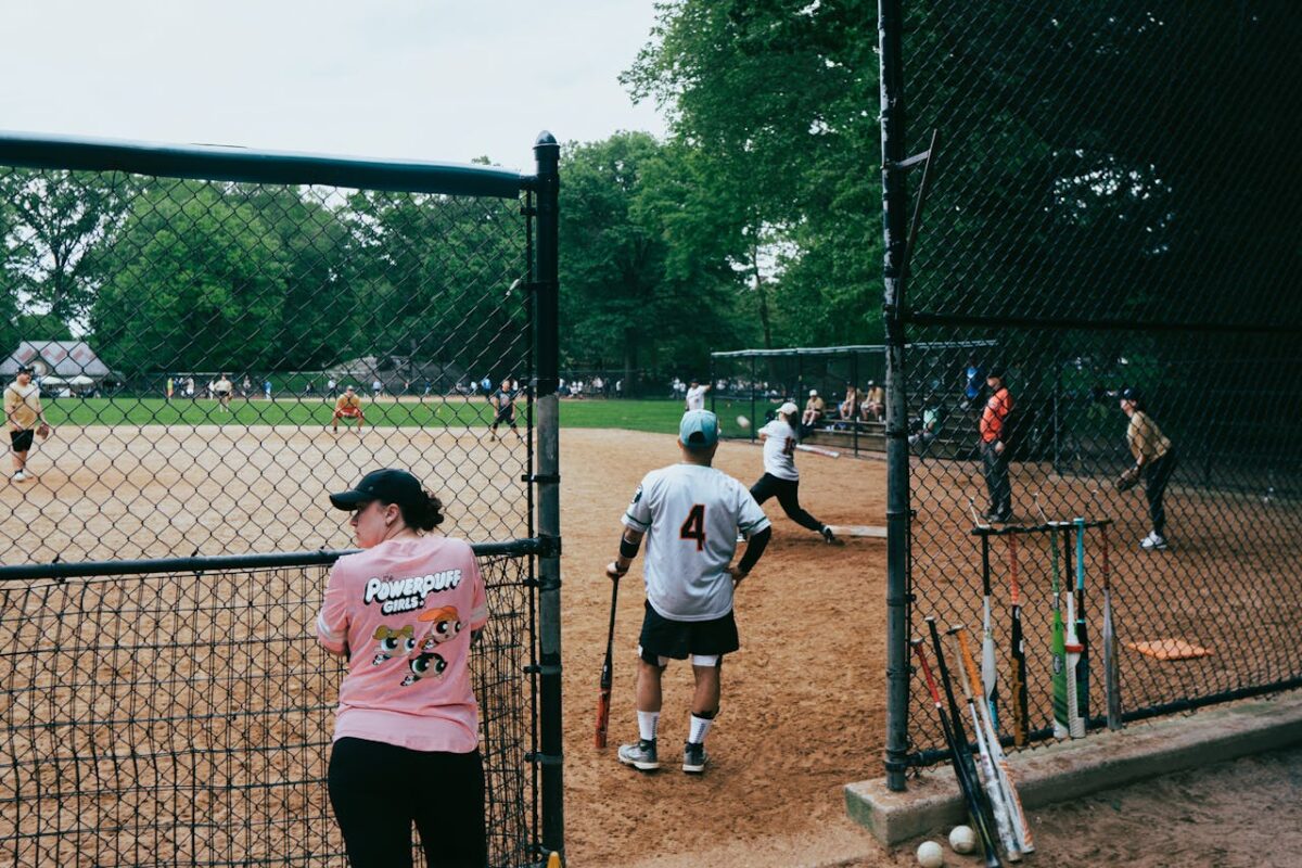 A casual baseball game in a New York City park with players and spectators on a sunny day.